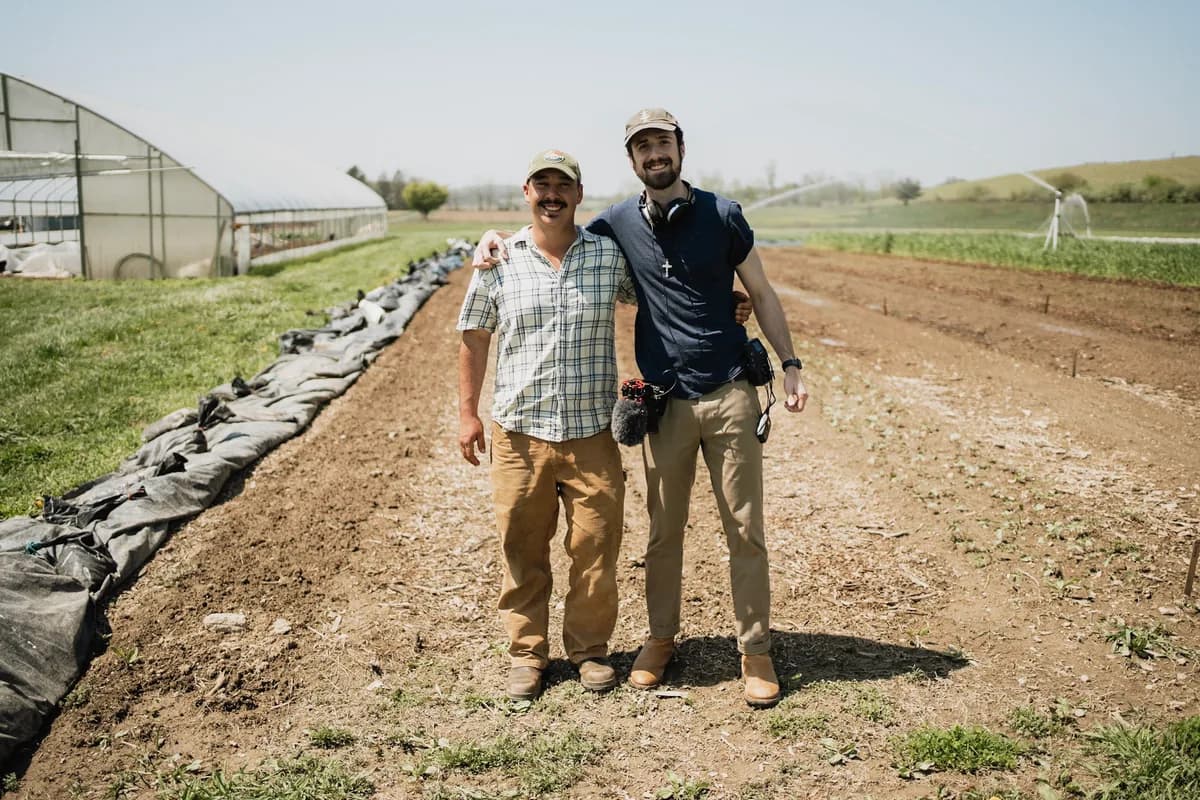 Jack Dempsey on a farm visit beside growing beds and a greenhouse